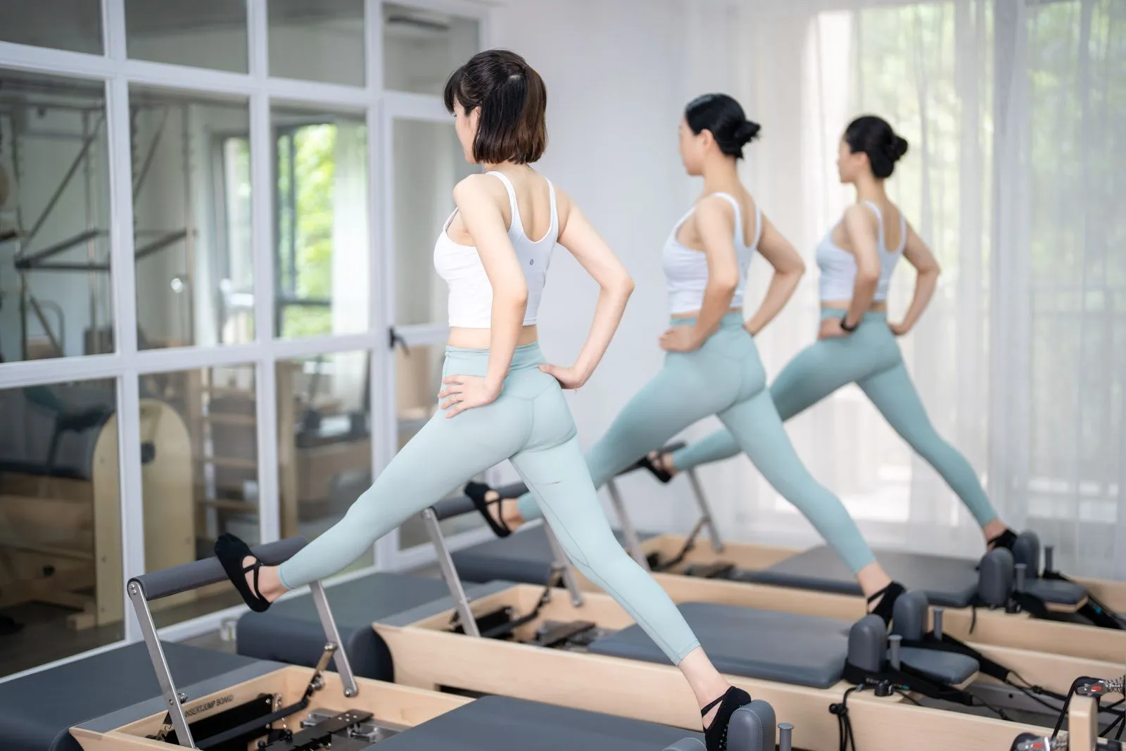 Three women in athletic wear exercising on Pilates reformers indoors, promoting a healthy lifestyle.